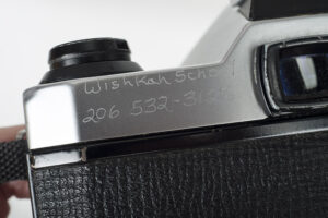 Photo of the rear corner of a Pentax K1000, with "Wishkah School" and a phone number engraved on it.